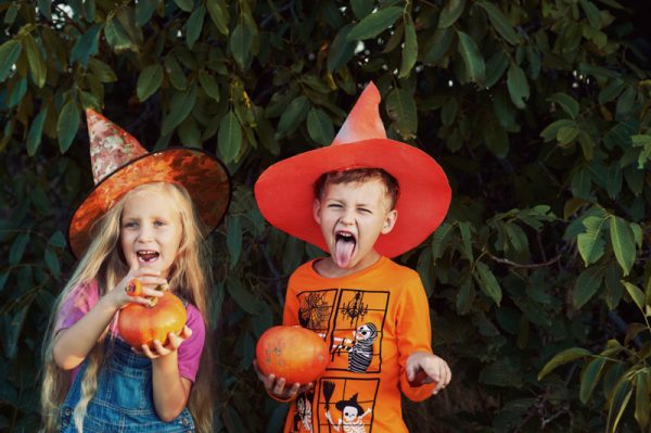 Kids dressed up for Halloween holding pumpkins and having fun outside.