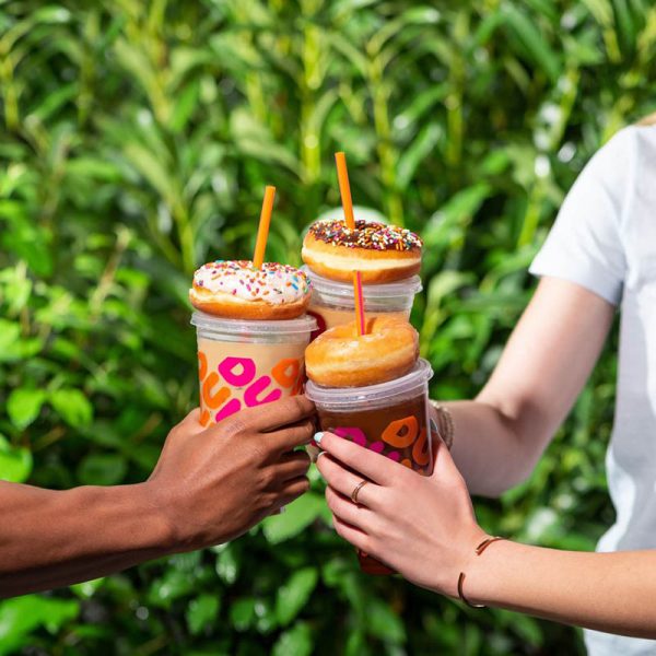 three people hold dunkin donuts cups topped with donuts